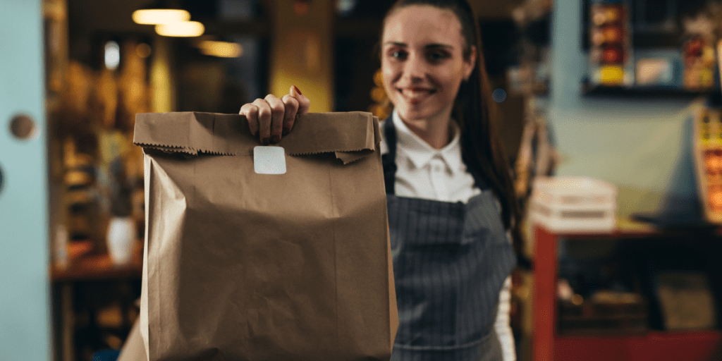 Vendeuse qui tend un sac kraft pour vente à emporter