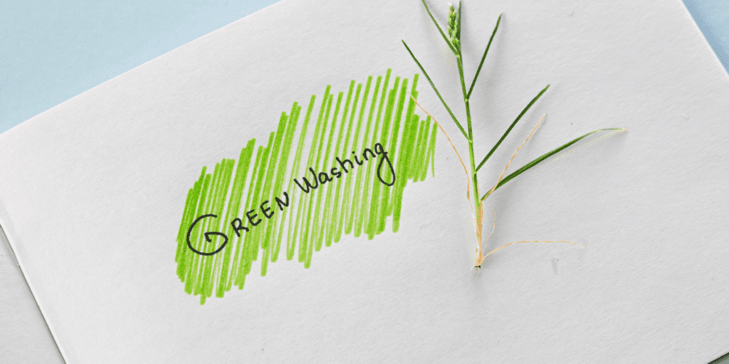 Feuille Blanche avec écrit greenwashing en noir sur fond vert et un brin d'herbe à côté