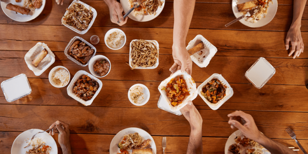 Plusieurs personnes qui partagent des repas de vente à emporter disposés sur une table en bois