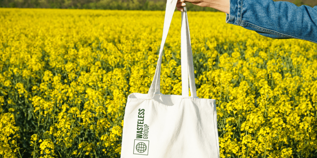 Tote-Bag en coton avec logo Wasteless Group tenu dans une main devant un champ de fleur jaune