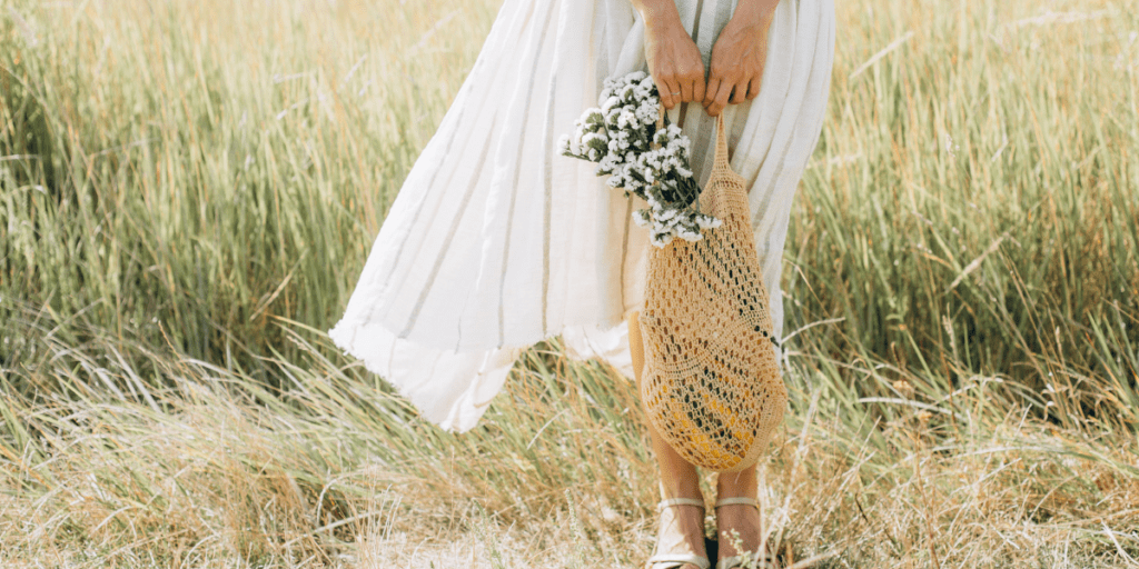 Femme en robe blanche tenant un sac de coton devant un champ