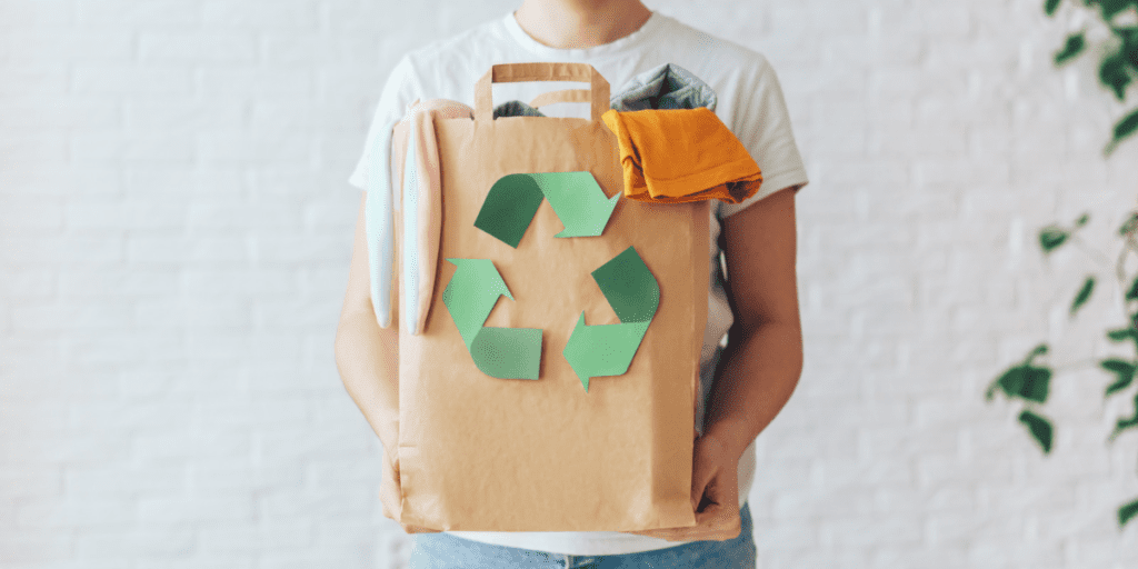 Personne tenant un sac en papier rempli d'habits avec le logo du recyclage